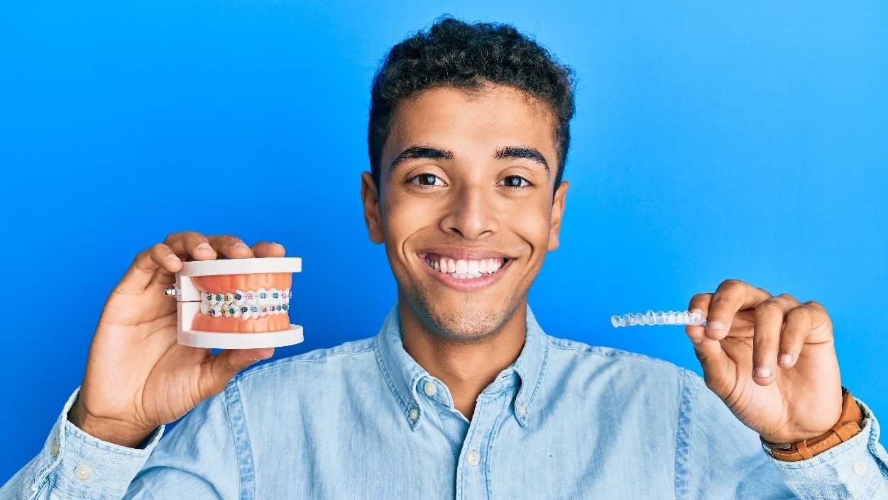 Invisalign Vs. Braces Man holding braces and Invisalign to compare