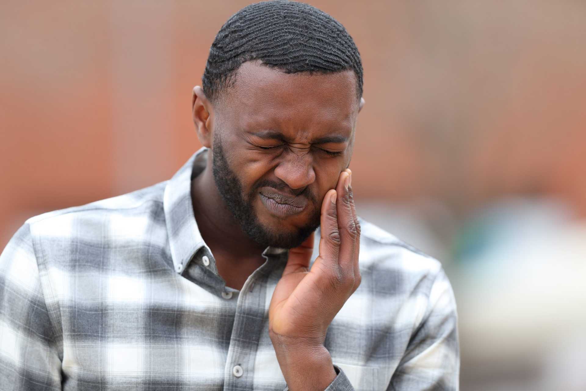 Front,view,portrait,of,a,man,with,black,skin,complaining Picture of man gripping cheek with mouth pain