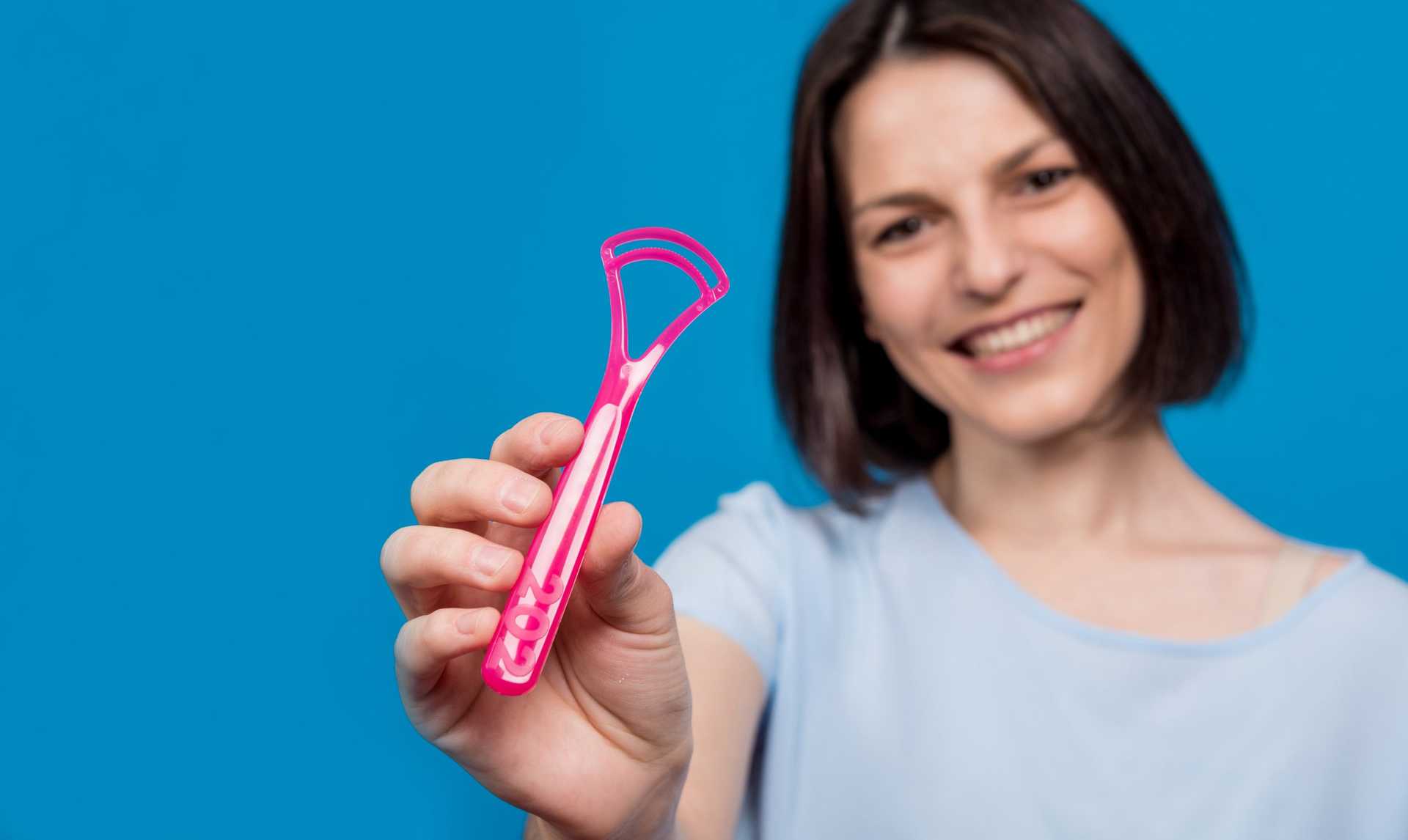 Beautiful,happy,young,woman,with,tongue,scraper,on,blank,blue Beautiful,happy,young,woman,with,tongue,scraper,on,blank,blue