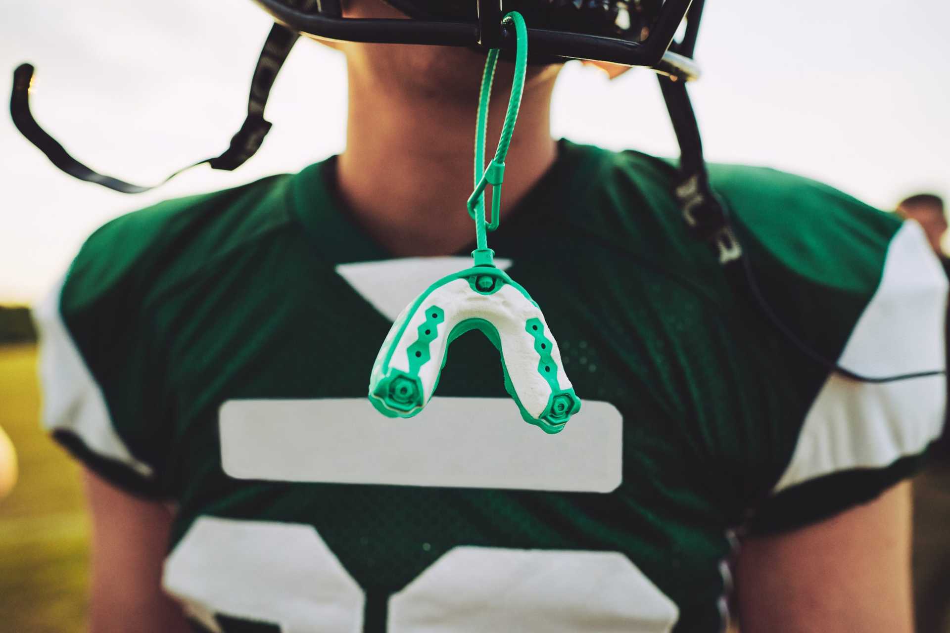 Closeup,of,a,mouthguard,hanging,off,the,helmet,of,an Boy in football jersey wearing helmet with mouth guard hanging down